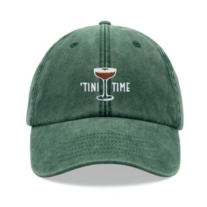 Puede incluir: Una gorra de béisbol verde con el texto "'TINI TIME" bordado en blanco y un pequeño gráfico de vaso de cóctel marrón y blanco.