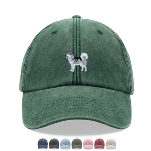 May include: A forest green baseball cap featuring an embroidered graphic of a standing husky dog with grey, white, and black fur. The cap has a structured crown, a curved brim, and a series of small ventilation eyelets on the upper panels.