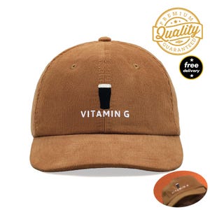 May include: A tan corduroy baseball cap featuring an embroidered graphic of a black pint glass with white foam and the text VITAMIN G in white capital letters centred on the front panel. The cap has a structured crown and a curved brim.