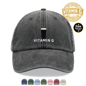 May include: A charcoal grey baseball cap with a distressed finish, featuring an embroidered graphic of a dark stout beer in a glass above the white text VITAMIN G centred on the front panel, with a curved brim and six-panel construction.