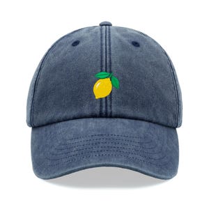 Pode incluir: Um boné de beisebol de denim azul escuro com um design de limão bordado.