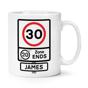 May include: White ceramic mug featuring a black and white graphic of a road sign. The sign reads "30 Zone Ends" with a red circle around the number 30 and a smaller red circle with the number 20 crossed out. The name "JAMES" is printed below the sign.