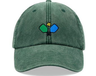 Puede incluir: Una gorra de béisbol de algodón verde oscuro, ajustable, con un diseño bordado de dos palas de pickleball y una pelota.