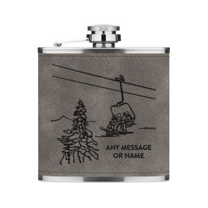 Puede incluir: Una petaca de acero inoxidable gris con un acabado de cuero. Presenta una silueta negra de un telesilla con personas que viajan en la góndola. El texto "ANY MESSAGE OR NAME" está grabado debajo de la imagen.