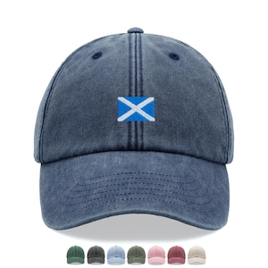 May include: A navy blue baseball cap with a distressed, washed-out finish. The front panel features an embroidered rectangular patch displaying the blue and white Saltire flag of Scotland. The cap has a curved brim and a structured six-panel design.