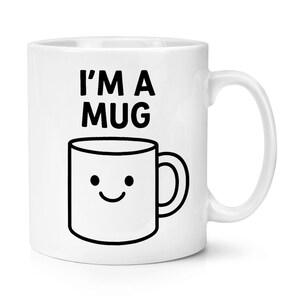 May include: White ceramic mug featuring a black outline of a smiling mug and the text "I'M A MUG". The mug has a curved handle and a simple design, suitable for hot beverages like tea or coffee.