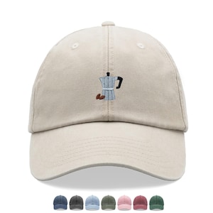 May include: A beige baseball cap with a curved peak. The cap has an embroidered design of a silver coffee maker and two brown coffee beans. The image shows the cap with a selection of other colour options.