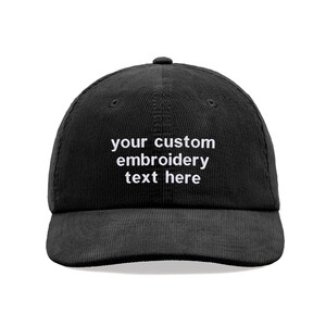 May include: A black corduroy baseball cap featuring the white embroidered text your custom embroidery text here centred on the front panel. The hat has a structured crown, a curved brim, and a button at the top of the cap.