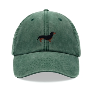 Könnte beinhalten: Eine grüne, abgenutzte Baseballkappe aus Baumwolle mit einer gestickten Dackel-Silhouette in Schwarz und Braun.