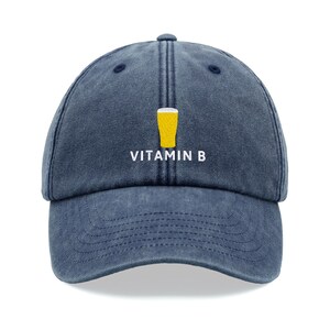 Può includere: Un cappello da baseball in denim blu con una grafica di un bicchiere di birra giallo e il testo "VITAMIN B" ricamato sul davanti.
