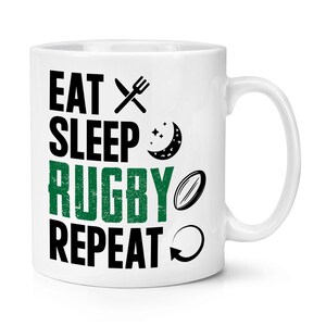 May include: White ceramic mug with black text that reads "Eat Sleep Rugby Repeat" with a fork and knife, a crescent moon, a rugby ball, and a circular arrow.
