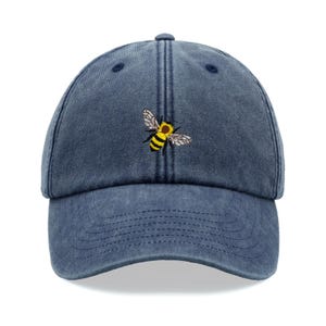 Peut inclure: Une casquette de baseball en denim bleu avec une abeille jaune et noire brodée sur le devant.