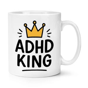Może przedstawiać: Biały ceramiczny kubek z czarnym napisem "ADHD KING", zwieńczony żółtą koroną. Kubek ma zakrzywiony uchwyt i jest przeznaczony do gorących napojów.