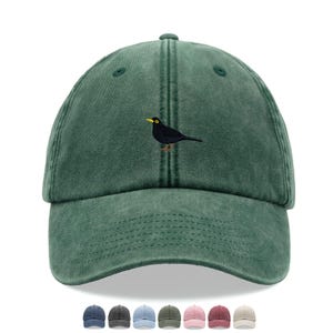 Puede incluir: Gorra de béisbol verde con un pájaro negro bordado en la parte delantera. El pájaro tiene un pico y un ojo amarillos. La gorra está hecha de un material de algodón lavado y tiene una visera curva. Se muestran varias otras opciones de color debajo.