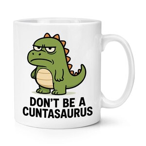 Puede incluir: Taza de cerámica blanca con un dibujo de un dinosaurio verde y naranja con una expresión de enfado. El texto "DON'T BE A CUNTASAURUS" está impreso en negro debajo. Un regalo divertido.