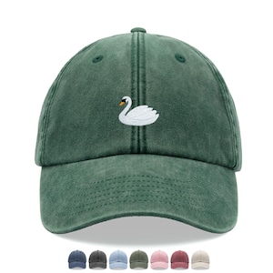 Puede incluir: Una gorra de béisbol de algodón verde desgastada con un cisne blanco bordado en la parte delantera.