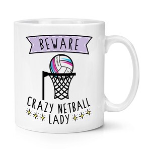 May include: White ceramic mug with a purple banner that says "BEWARE CRAZY NETBALL LADY" with a pink and blue netball in a net and gold stars.