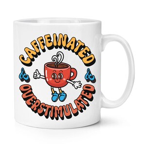 Op de afbeelding: Witte keramische koffiemok met een cartoon koffiekopje met een gezicht en de tekst "caffeinated & overstimulated" in een cirkel eromheen.