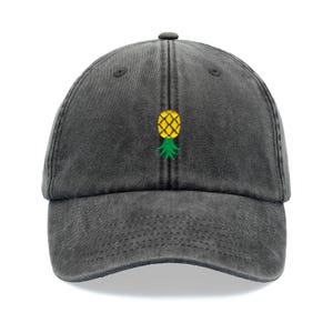 Könnte beinhalten: Eine schwarze Baseballkappe aus Denim mit einem gestickten gelben Ananas auf der Vorderseite.