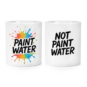 Puede incluir: Dos tazas de cerámica blancas. Una taza presenta las palabras "PAINT WATER" en negro, con un diseño de salpicaduras de pintura coloridas. La otra taza tiene las palabras "NOT PAINT WATER" en negro.