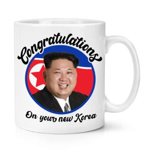 May include: White ceramic mug with a handle. The mug features a circular design with a portrait of a smiling man in a suit, set against a red, white, and blue background. The words "Congratulations" and "On your new Korea" are written on the mug.
