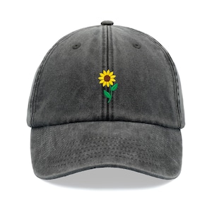 Puede incluir: Una gorra de béisbol de denim negro con un girasol amarillo bordado.