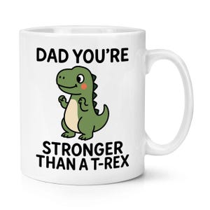Puede incluir: Taza de cerámica blanca con el texto "DAD YOU'RE STRONGER THAN A T-REX". La taza presenta una ilustración de dinosaurio de dibujos animados en verde, beige y rosa. La taza tiene un asa blanca y es adecuada para bebidas frías o calientes.