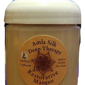 May include: A brown jar with a white lid and a label that says "Amla Silk Deep Therapy Restorative Masque 4 oz". The label also has a decorative design and the text "Lakshmi's Cupboard" and "Apply to wet/dry hair. Rinse."