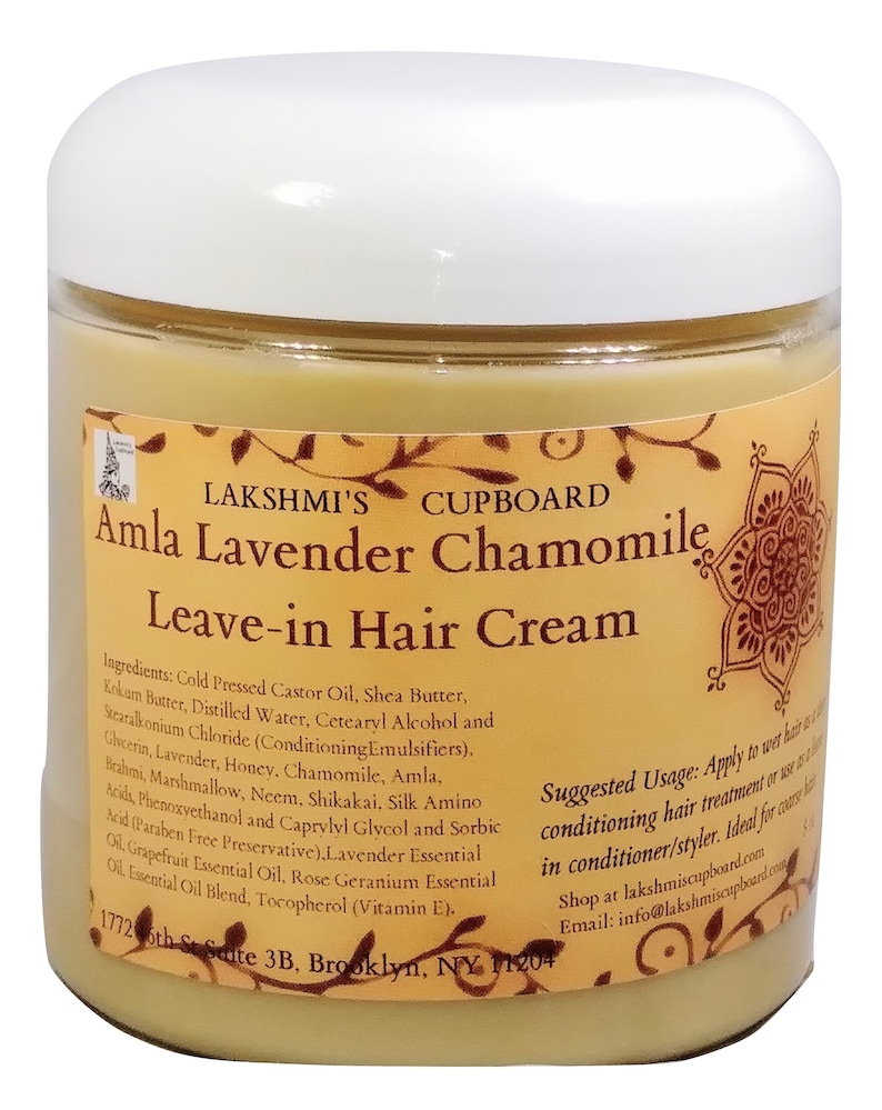 May include: A glass jar with a white lid containing a light yellow cream. The label is orange and brown with the text "LAKSHMI'S CUPBOARD Amla Lavender Chamomile Leave-in Hair Cream". The ingredients and suggested usage are listed on the label.