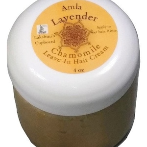 May include: A white jar with a gold lid and label. The label says "Amla Lavender Chamomile Leave-In Hair Cream" and "Lakshmi's Cupboard". The jar contains a light brown cream and is 4 oz.