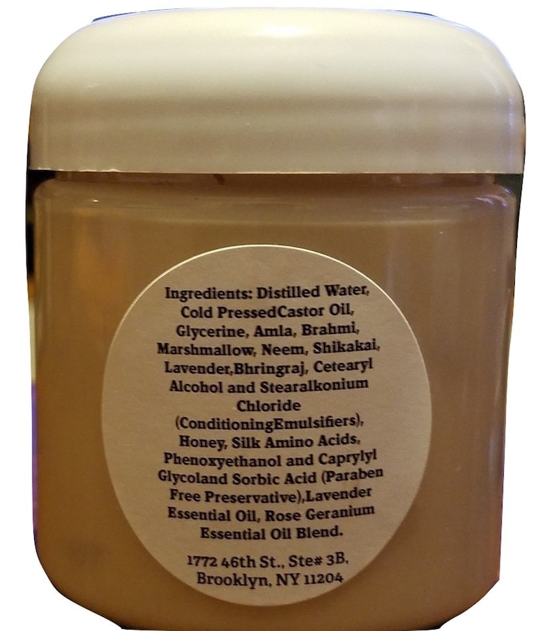 May include: A white plastic jar with a brown label listing the ingredients of a hair care product. The label includes the text "Ingredients: Distilled Water, Cold Pressed Castor Oil, Glycerine, Amla, Brahmi, Marshmallow, Neem, Shikakai, Lavender, Bhringraj, Cetearyl Alcohol and Stearalkonium Chloride (Conditioning Emulsifiers), Honey, Silk Amino Acids, Phenoxyethanol and Caprylyl Glycoland Sorbic Acid (Paraben Free Preservative), Lavender Essential Oil, Rose Geranium Essential Oil Blend. 1772 46th St., Ste# 3B, Brooklyn, NY 11204"