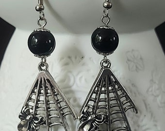 May include: A pair of silver spiderweb earrings with black beads. Each earring features a detailed spiderweb design with a small spider at the bottom.