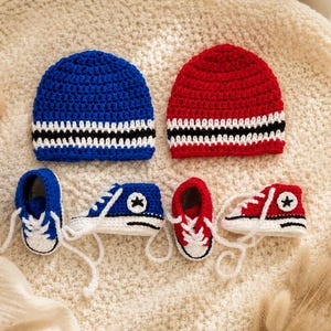 May include: A set of two crocheted beanies and two pairs of crocheted sneakers. One beanie is blue with white and black stripes, and the other is red with white and black stripes. The sneakers match the beanies, featuring white laces and star logos.