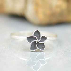 May include: A silver ring with a black flower design.