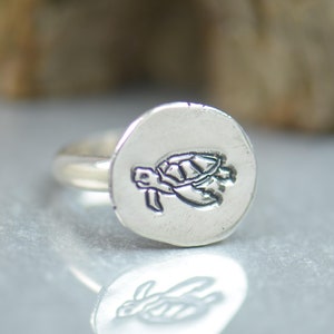 Op de afbeelding: Een zilveren ring met een schildpad ontwerp. De ring is rond en heeft een glad oppervlak.
