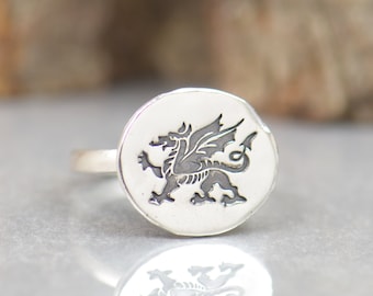 May include: A silver ring with a round, engraved design featuring a black dragon. The ring is on a white surface.
