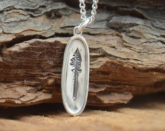 May include: A silver necklace with a pendant featuring an engraved pine tree design. The pendant is oval shaped and hangs from a silver chain.