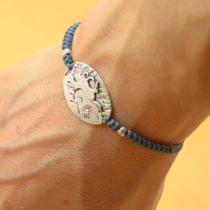 May include: A silver charm bracelet with a detailed design of a mythical creature on a round charm. The bracelet is made of dark blue cord.