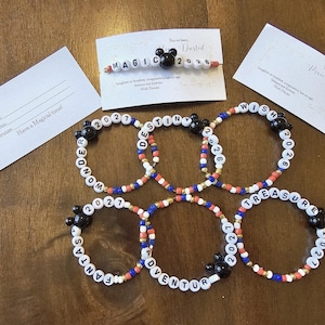 May include: A collection of beaded bracelets with white letter beads spelling out words like "WONDER", "DESTINY", and "TREASURE". Each bracelet has a black Mickey Mouse head bead. Small cards with text are also present.