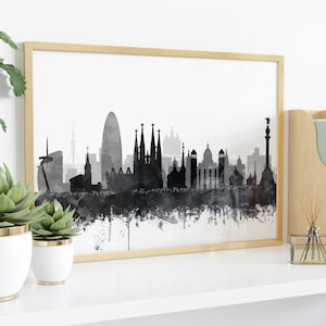 K&ouml;nnte beinhalten: Schwarz-wei&szlig;es Aquarell-Stadtbild von Barcelona, Spanien, gerahmt in einem goldenen Rahmen und auf einem wei&szlig;en Regal mit Pflanzen und Dekorationen ausgestellt.
