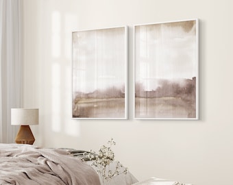 Pode incluir: Duas pinturas abstratas de aquarela em tons de marrom suaves, emolduradas em branco, penduradas em uma parede bege claro acima de uma cama com um edredom branco e um cobertor de lã marrom.