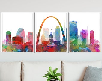 Op de afbeelding: Een aquarel van de skyline van St. Louis, met de iconische Gateway Arch. Het schilderij is verdeeld in drie panelen, met de boog in het middelste paneel en de skyline van de stad aan weerszijden. Het schilderij is gemaakt in een levendig kleurenpalet, waaronder rood, oranje, geel, groen, blauw en paars.