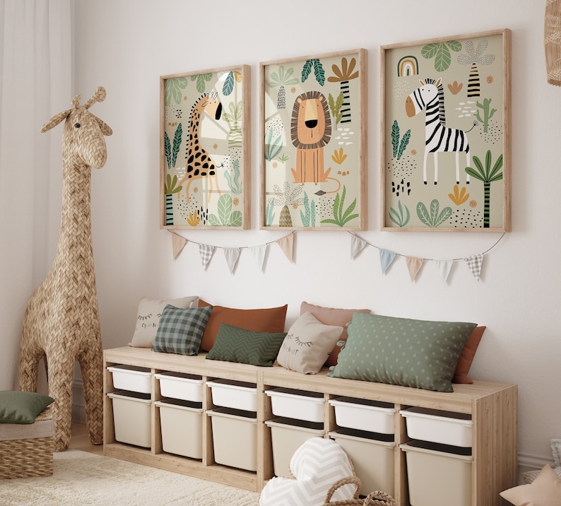 Op de afbeelding: Een set van drie ingelijste illustraties met een giraffe, leeuw en zebra in een jungle-omgeving. De illustraties zijn in cartoon-stijl en hebben een heldere, kleurrijke palette. De frames zijn van hout en hebben een natuurlijke afwerking.