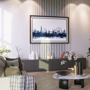 May include: A modern living room interior with a gray sofa, a coffee table, and a framed watercolor painting of the London skyline. The painting is hanging on a wall with vertical wood panels. There are plants and decorative vases on the shelves below the painting.