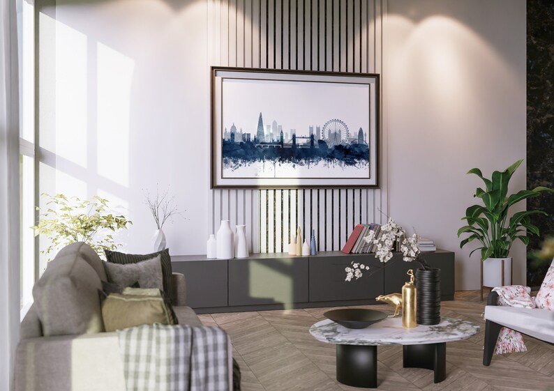 May include: A modern living room interior with a gray sofa, a coffee table, and a framed watercolor painting of the London skyline. The painting is hanging on a wall with vertical wood panels. There are plants and decorative vases on the shelves below the painting.