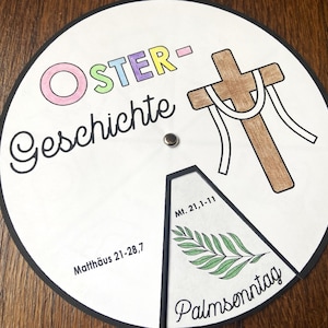 Könnte beinhalten: Ein weißes, kreisrundes Papierrad mit schwarzem Rand. Das Rad hat einen bunten Titel "OSTER-Geschichte" und ein Bild eines Kreuzes mit einem Seil darum. Das Rad ist in Abschnitte mit Text und Bildern unterteilt, darunter "Matthäus 21-28,7", "Mt. 21,1-11" und "Palmsonntag".