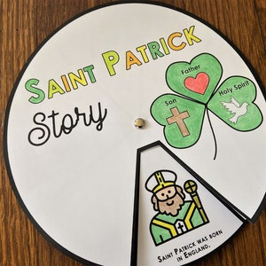 May include: A white paper wheel with the words "Saint Patrick Story" in green, yellow, and orange. The wheel features a green shamrock with a red heart, a cross, and a white dove. The wheel also has a picture of Saint Patrick wearing a green robe and holding a yellow staff. The text "Saint Patrick was born in England" is at the bottom of the wheel.