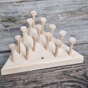 May include: A wooden triangular game board with 15 wooden pegs arranged in a pyramid shape. The pegs are all the same size and shape, and they are made of natural wood.