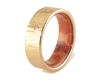 May include: A gold-colored ring with a hammered texture on the exterior and a reddish-brown wooden interior. The ring is a band style, showcasing a contrast of materials and textures.
