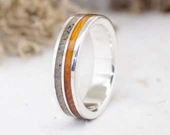 Op de afbeelding: Een zilveren ring met een dunne inleg van hout en zand.